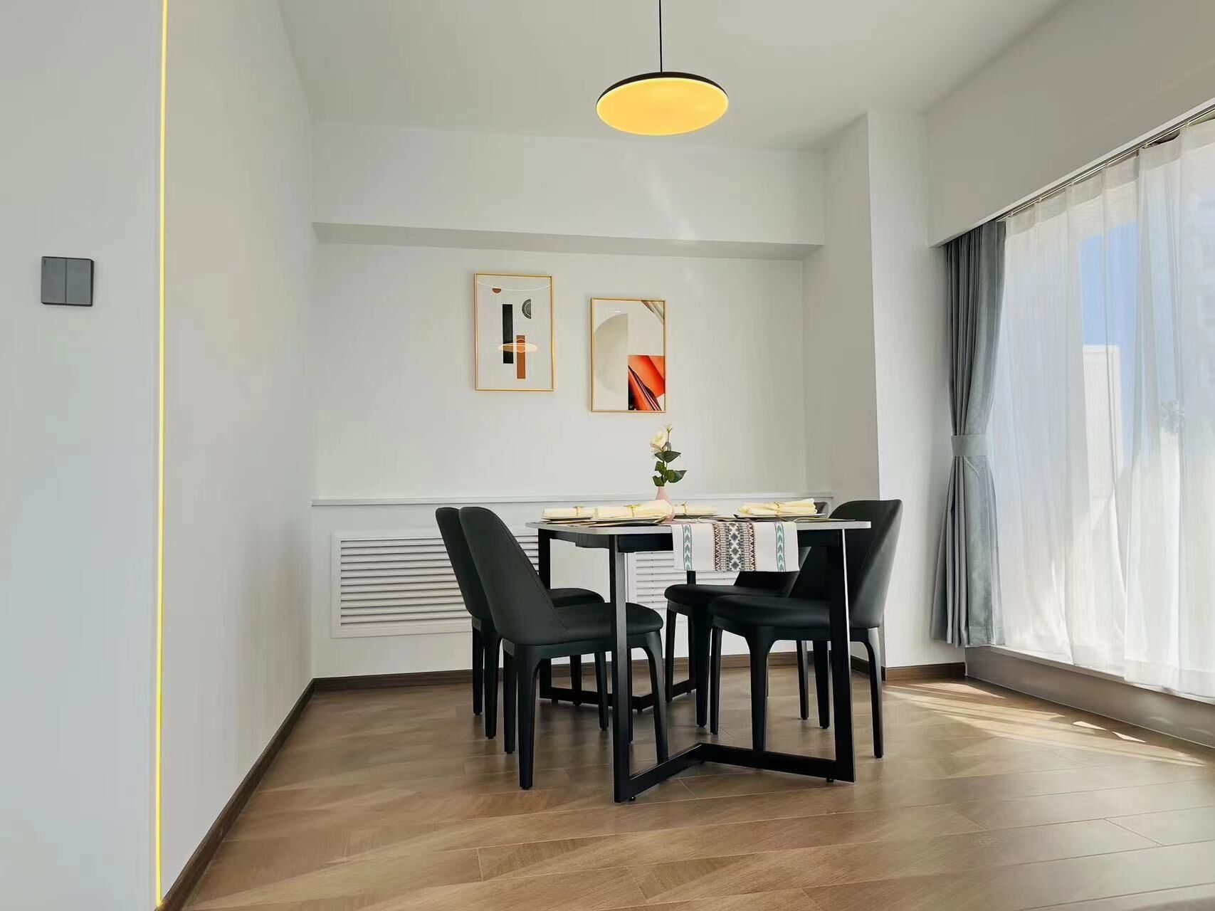 Un comedor con una mesa dispuesta para cuatro, una lámpara colgante y dos obras de arte enmarcadas en la pared.