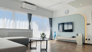 A modern hotel room with a large window, a flat-screen TV, a bedside table, and a built-in air conditioning unit. - Beijing Jiuxian Apartment (Beijing)