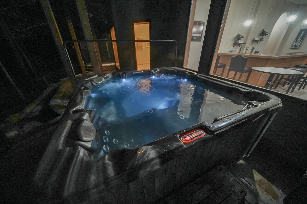 A hot tub with a visible logo, surrounded by a glass enclosure, with a bar area visible through the glass in the background.