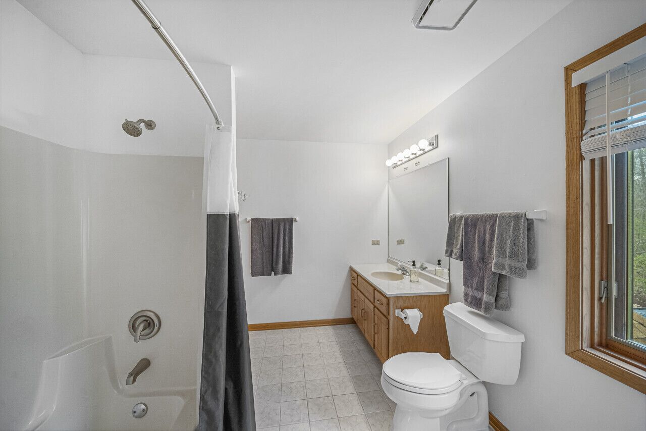 A modern bathroom with a shower, toilet, vanity, and a large mirror with lights.