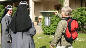A courtyard with a building in the background, a metal table, and a person with a red backpack. - Birgittasystrarnas Gästhem (Vadstena)