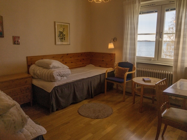 Un dormitorio acogedor con una cama de madera, una silla, una mesita y vistas al agua a través de una ventana.