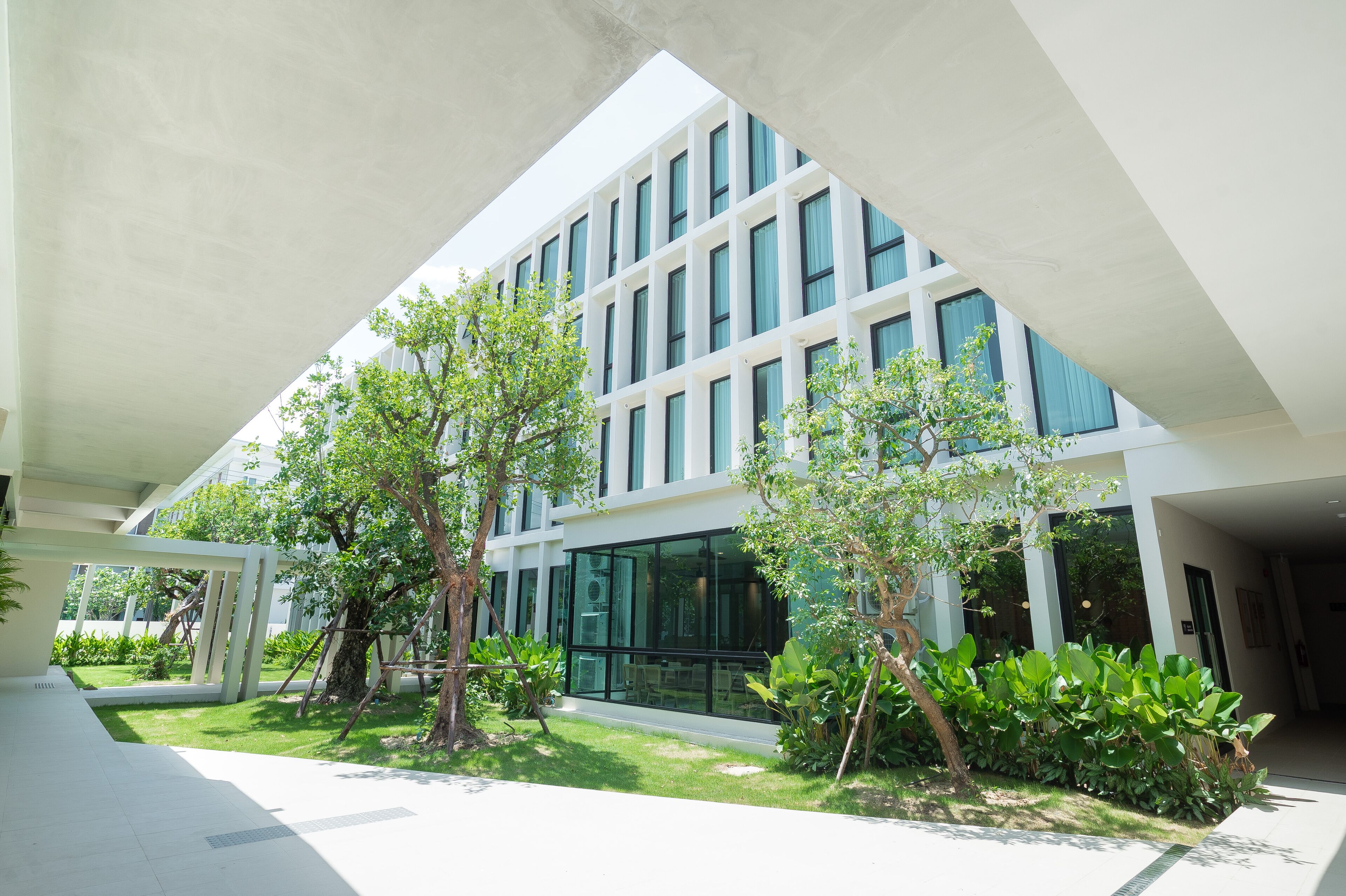 A modern building with a glass facade, surrounded by greenery and a covered walkway.