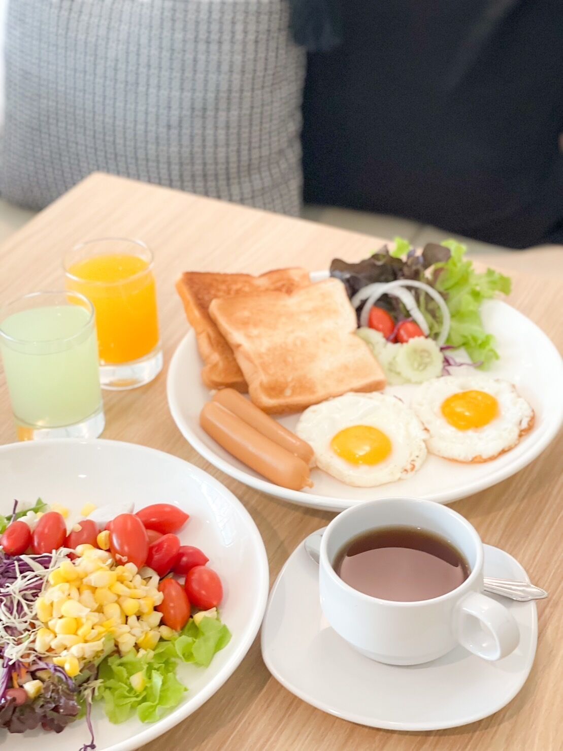 A breakfast setting with toast, eggs, sausages, a salad, and two drinks on a table.
