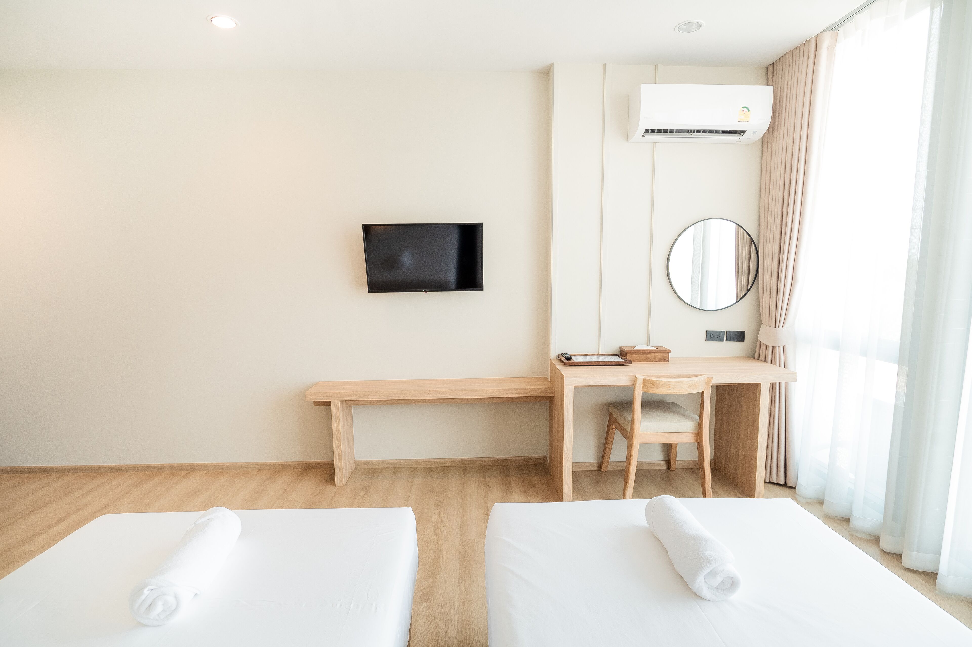 Ein Hotelzimmer mit zwei Betten, einem Schreibtisch, einem Sessel, einem Fernseher, einem Spiegel und einer Klimaanlage.