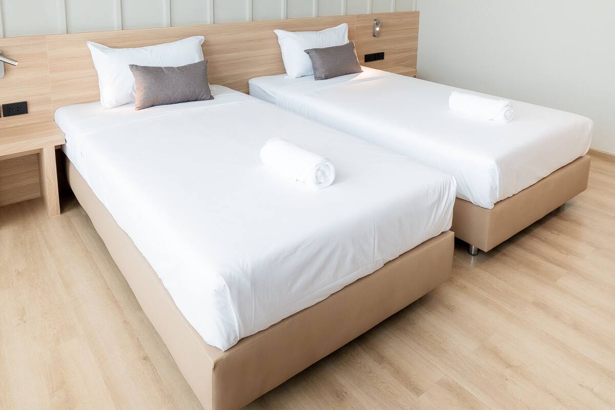 Camera d'albergo moderna con due letti singoli, una testiera in legno, un comodino e un pavimento in legno chiaro.