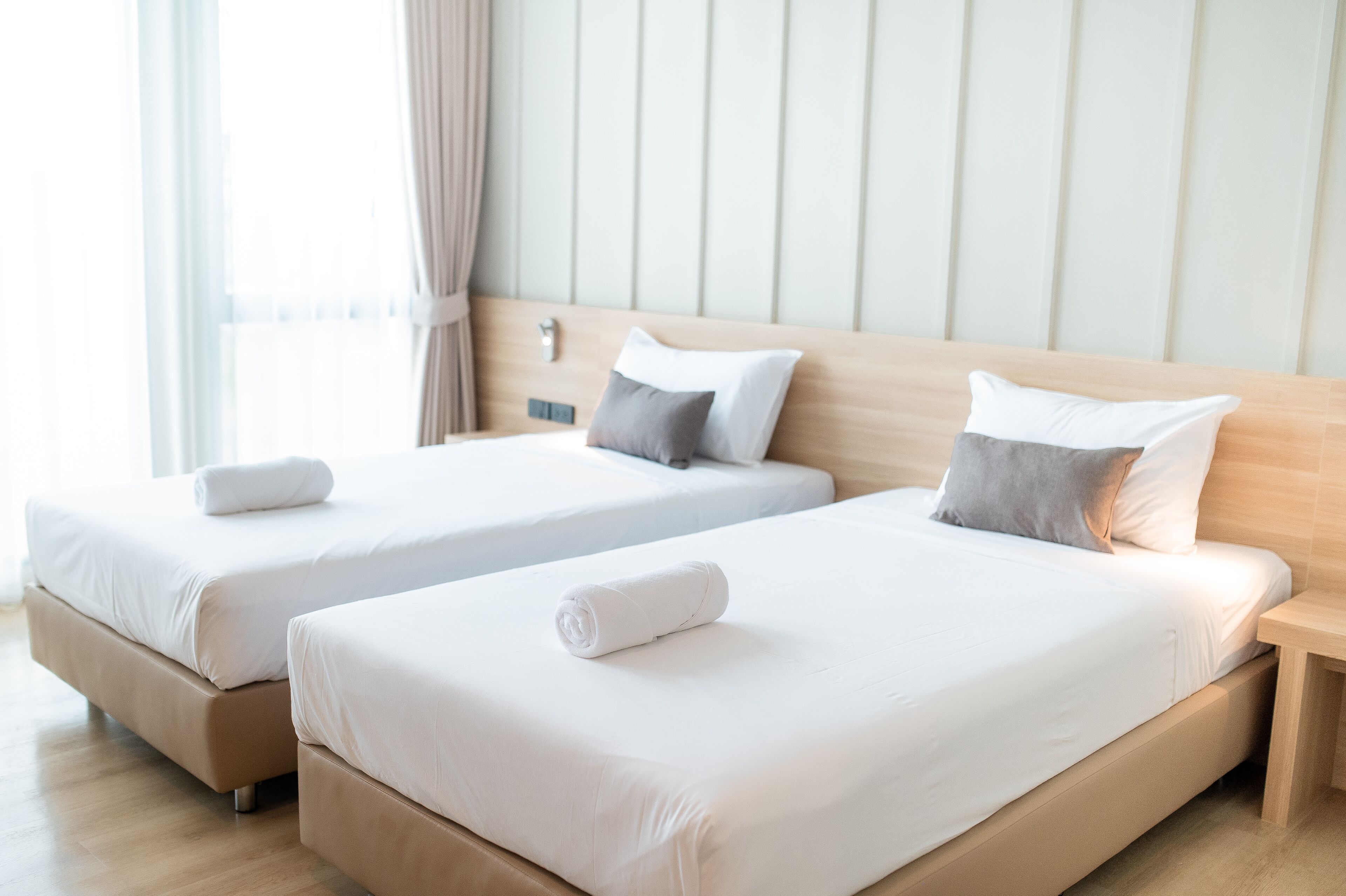 Two single beds with white linens and pillows, wooden headboards, and a wooden floor.
