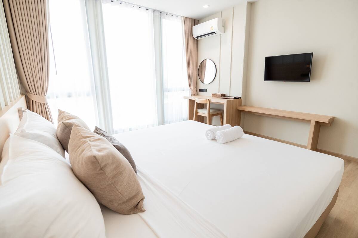 Camera d'albergo con un letto, una scrivania, una sedia, una TV e una finestra con tende.