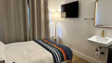 A hotel room with a bed, a bedside lamp, a TV mounted on the wall, and a sink with a mirror.