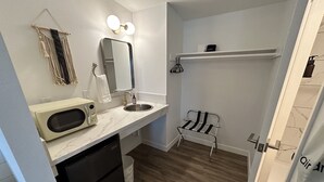 Ein kleines Badezimmer mit Waschbecken, Spiegel und einer Mikrowelle auf der Ablagefläche.