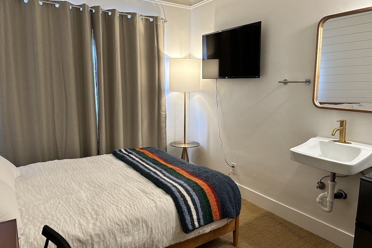 Ein Hotelzimmer mit Bett, Wandfernseher, Nachttischlampe und Waschbecken mit Spiegel.