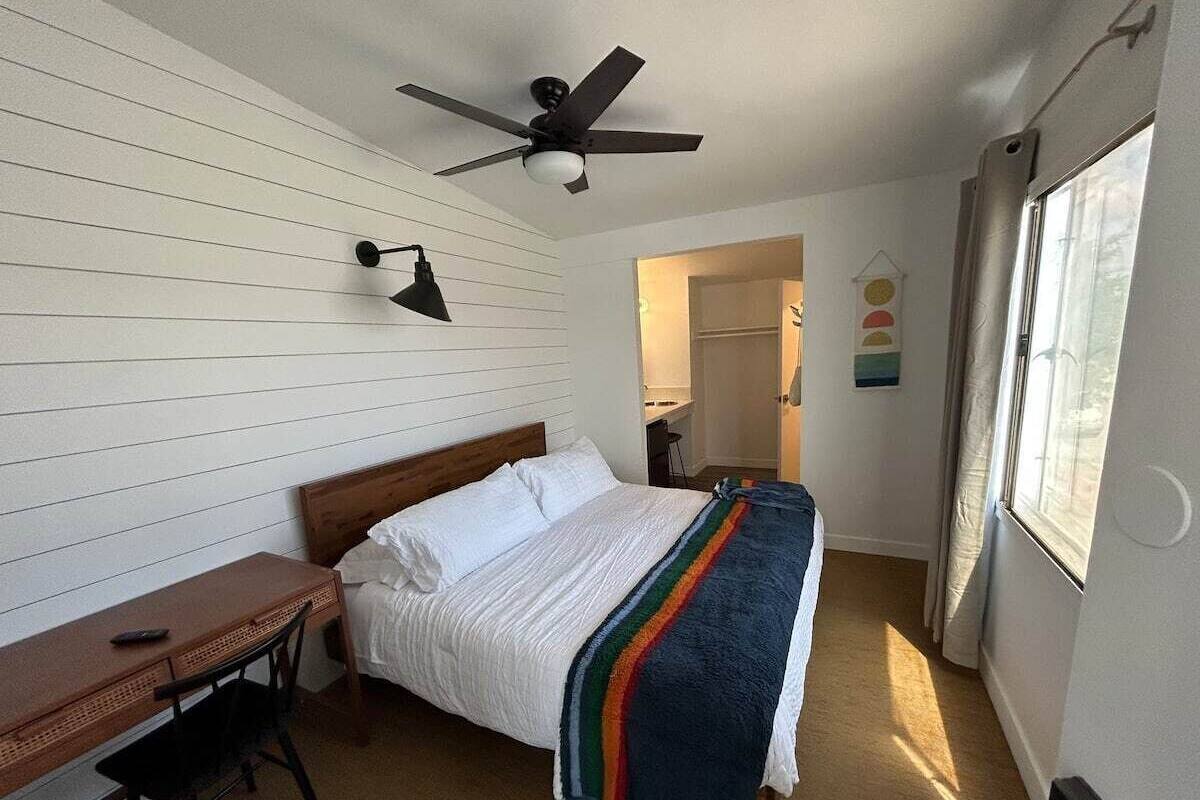 Ein Schlafzimmer mit Bett, Schreibtisch, Stuhl, Deckenventilator und Fenster.