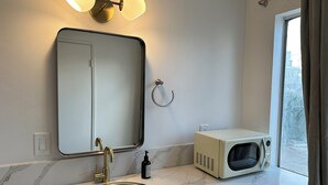 Ein Badezimmer mit Waschbecken, Spiegel und einer Mikrowelle auf der Arbeitsfläche.