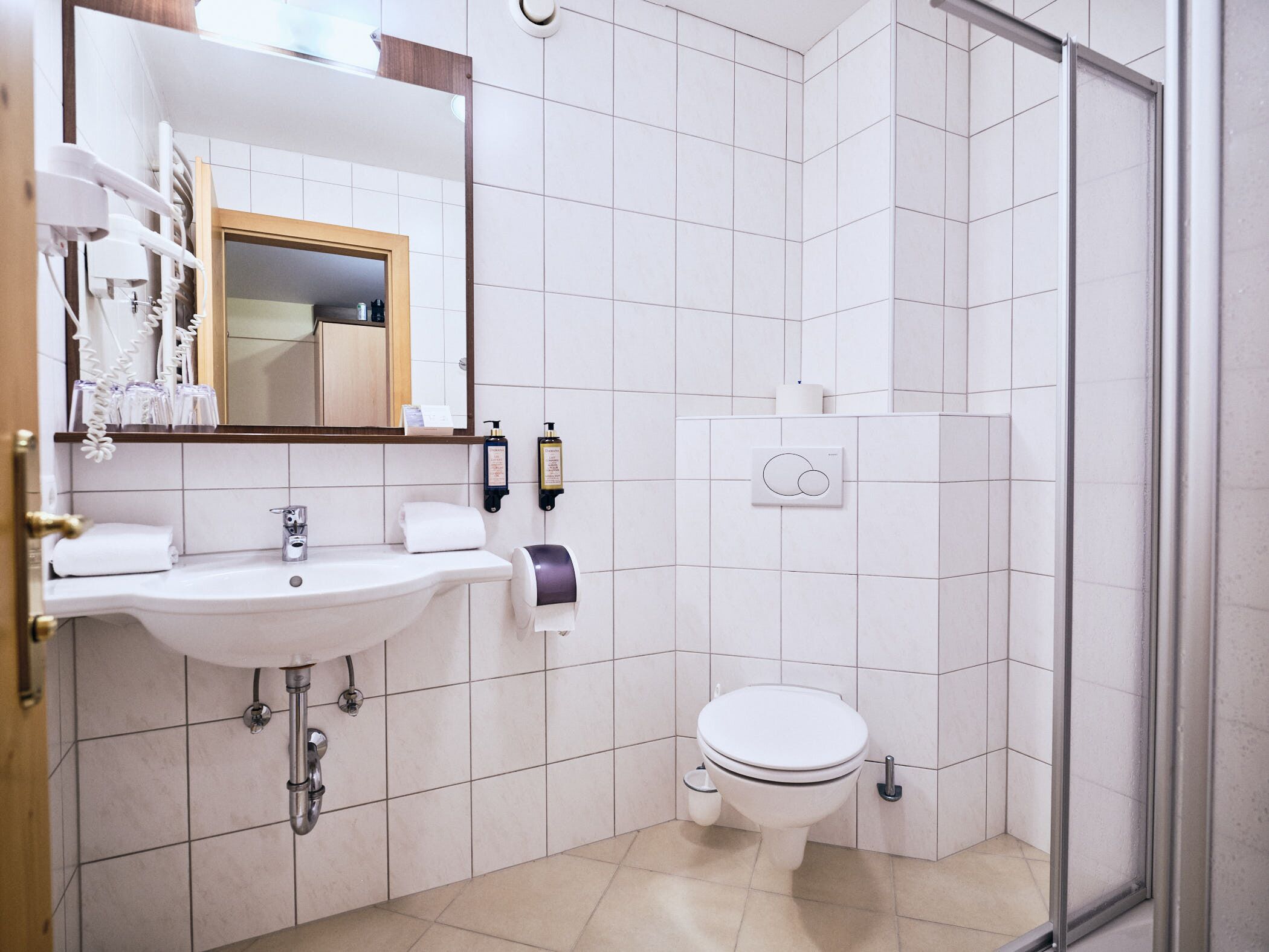 Et moderne badeværelse med håndvask, spejl, toilet og bruser.