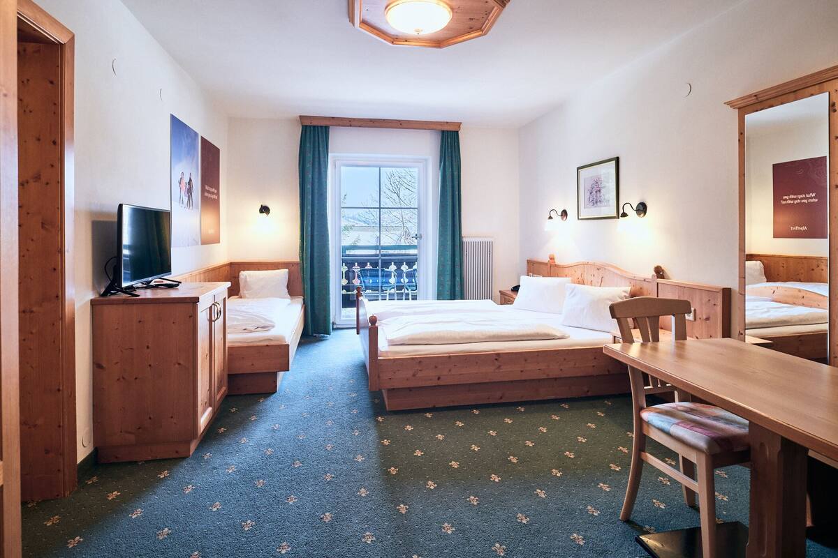 A hotel room with two beds, a desk, a chair, a TV, and a large window with a view.