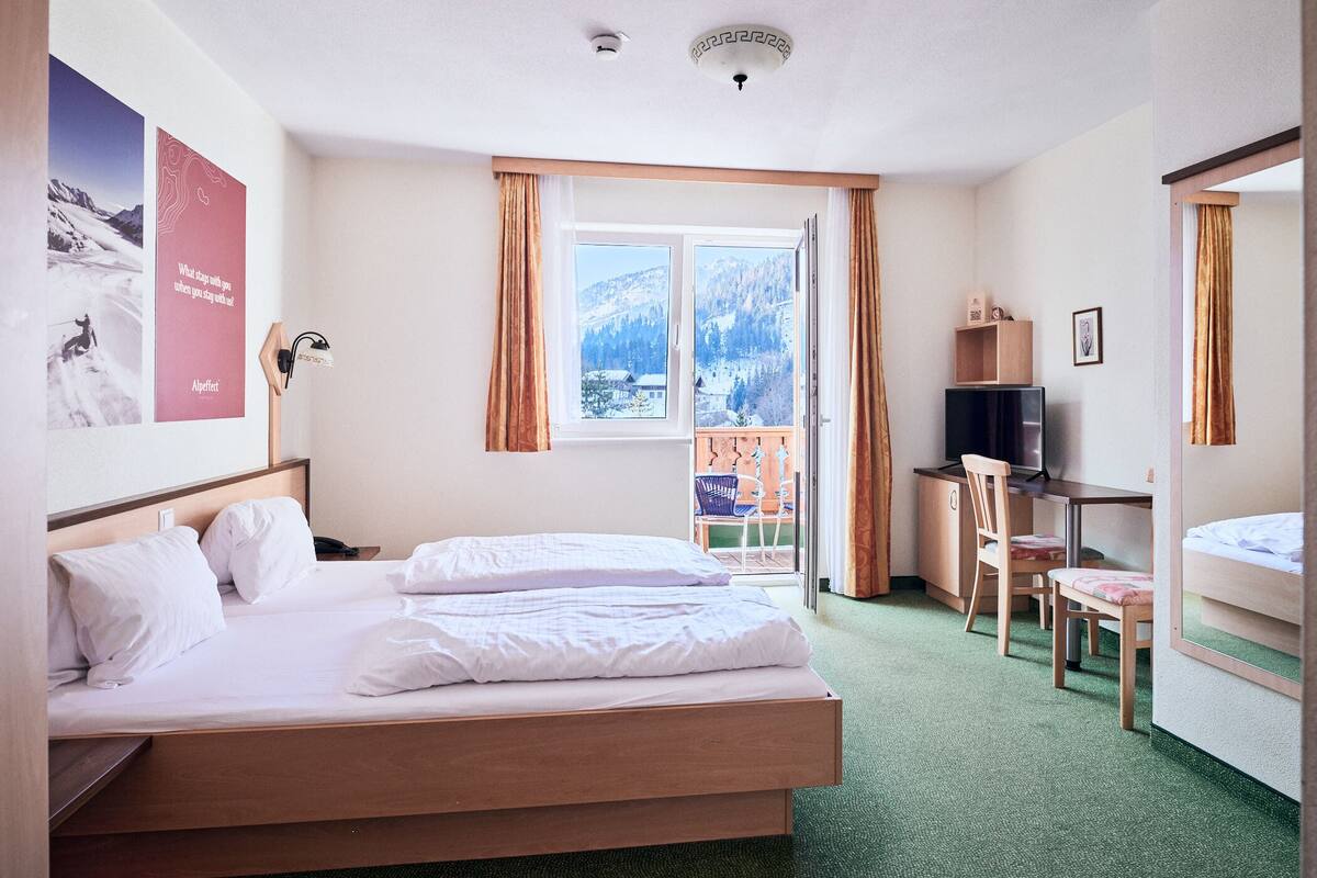 A hotel room with a bed, a desk with a chair, a TV, and a window with curtains.