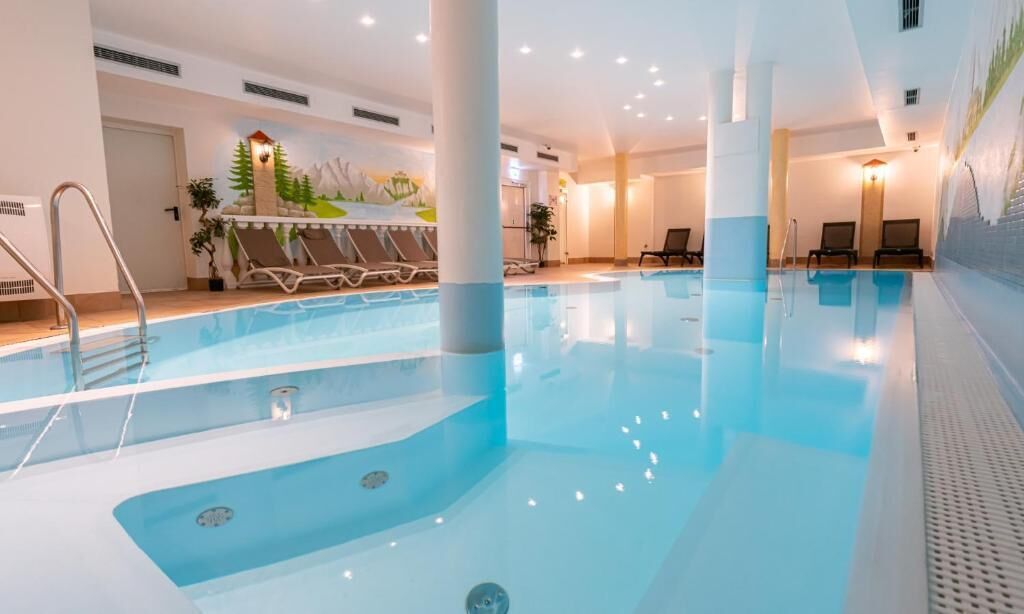 Una piscina interior con agua cristalina, sillones de descanso y un mural en la pared.
