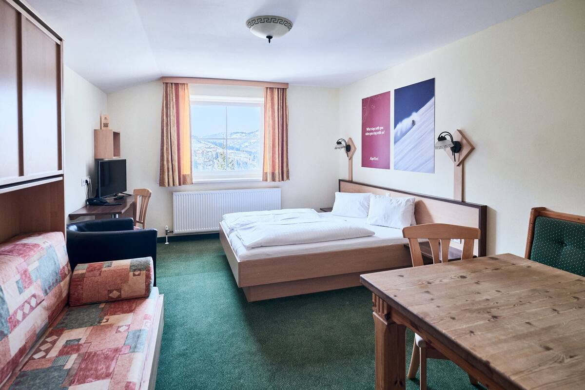 A hotel room with a bed, a desk, a chair, a sofa, a television, and a window with curtains.