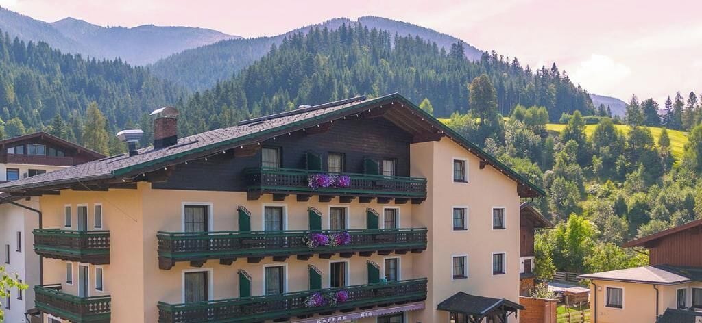 A multi-story building with balconies, set against a mountainous backdrop.