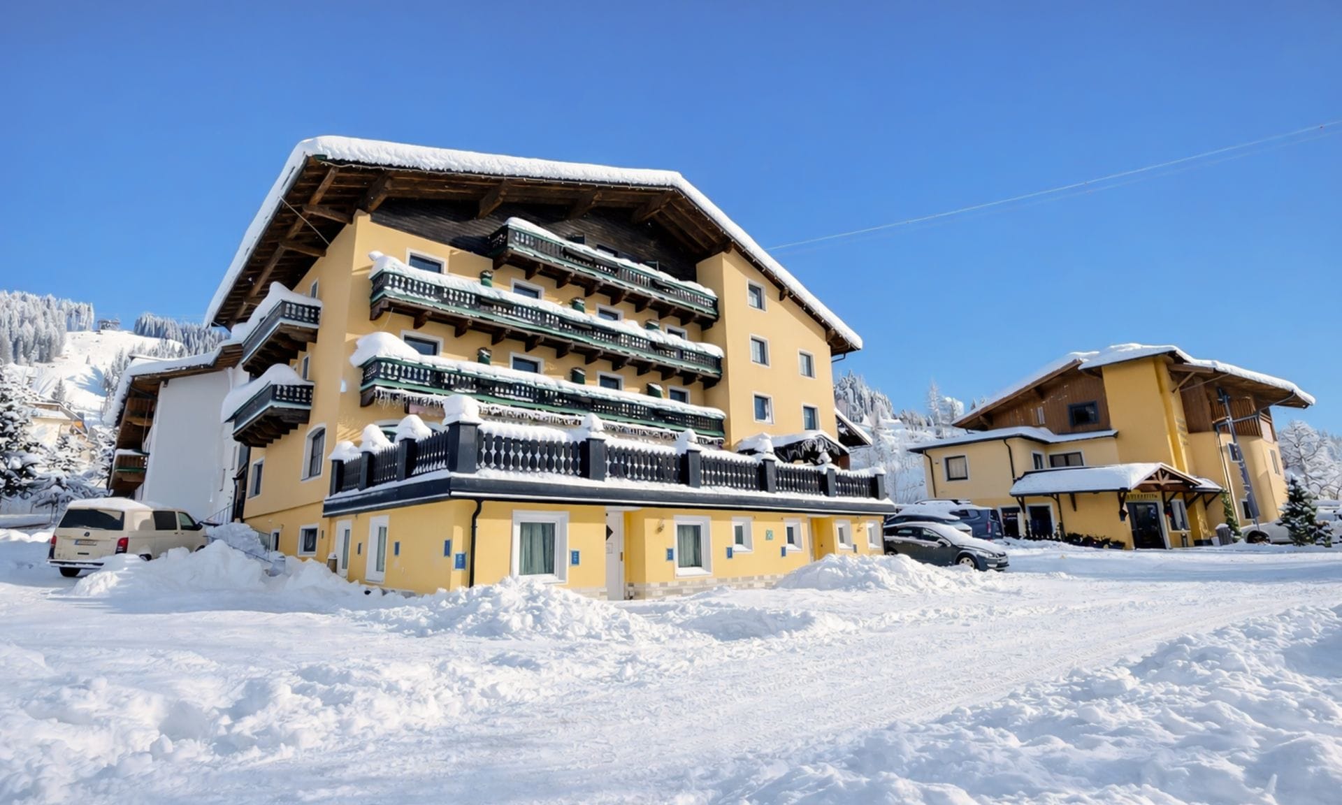Un hotel de varios pisos con balcones, una pista de esquí al fondo y un paisaje cubierto de nieve.