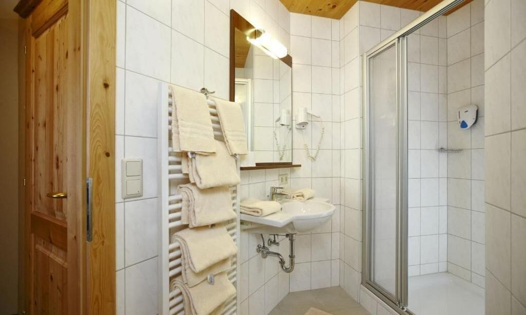 A bathroom with a wooden door, a towel rack, a sink, and a glass shower enclosure.