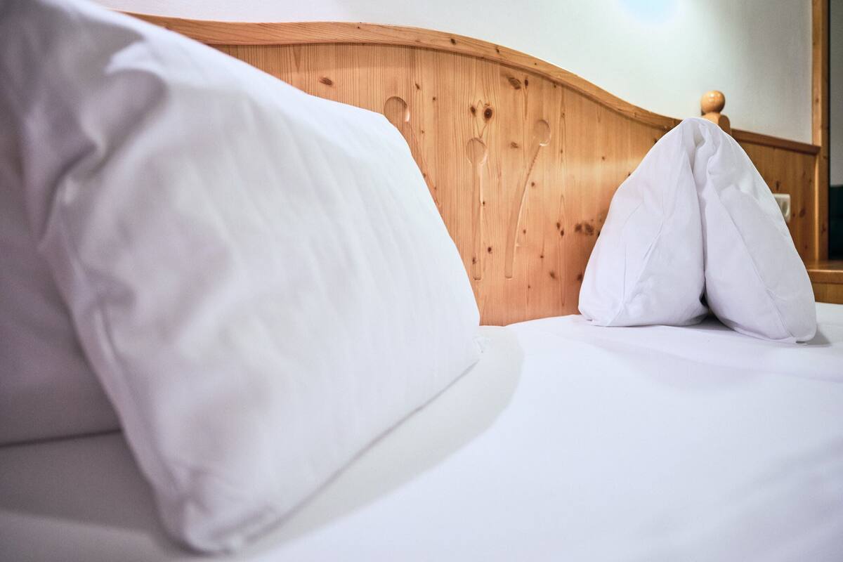 A neatly made bed with white linens and pillows, a wooden headboard, and a wooden wall paneling.