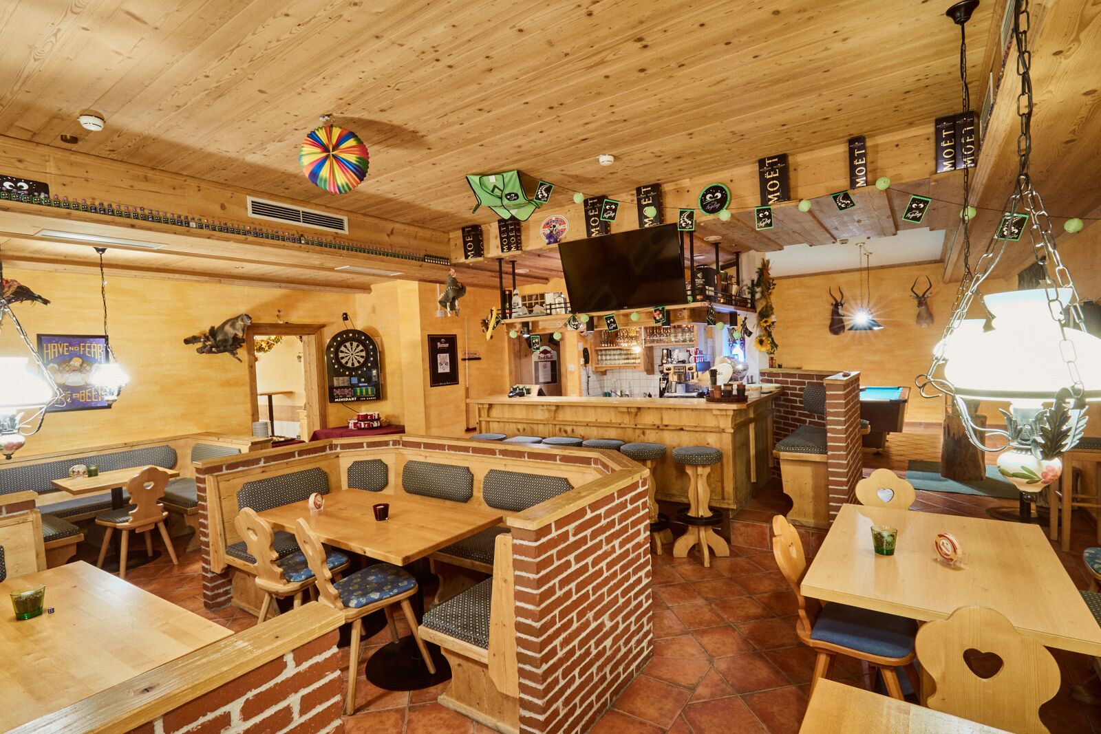 A cozy bar with wooden furniture, a dartboard, and a TV screen.