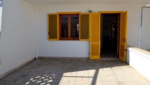 Ein Gebäude mit einer gefliesten Terrasse, einer weißen Außenwand und einer Tür mit gelben Rollläden.