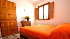 Ein Schlafzimmer mit einem Bett, einem Holzschrank, einem kleinen Tisch mit einer Vase und einem Fenster.