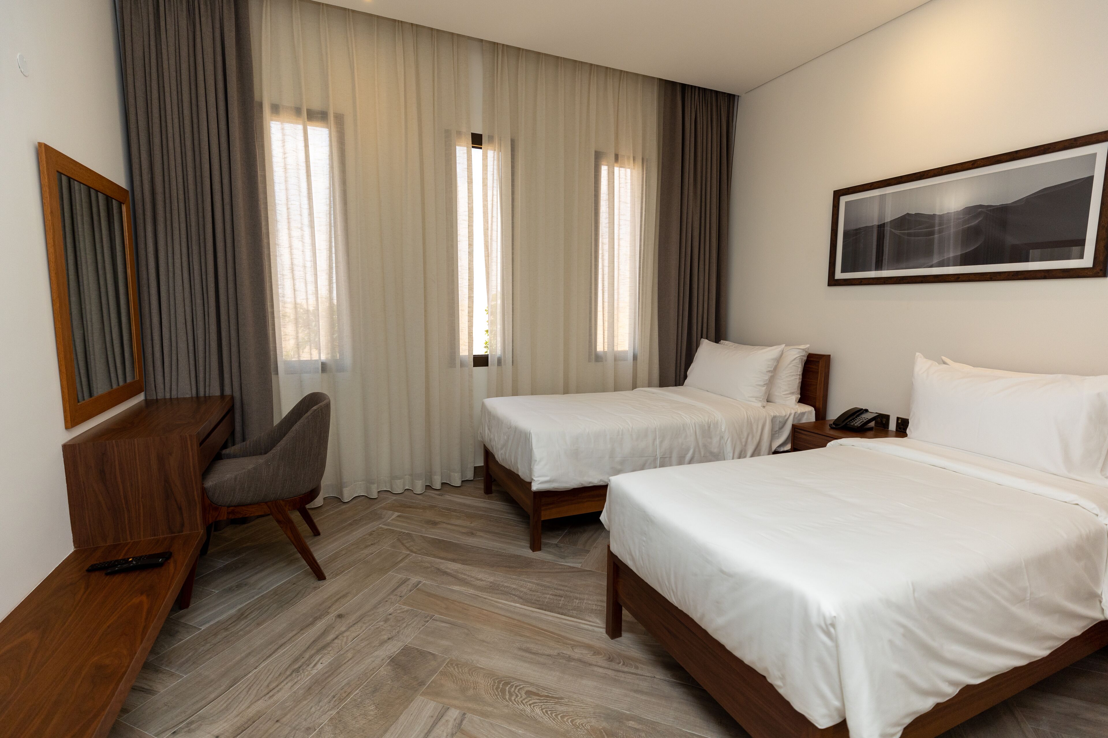 Une chambre d’hôtel avec deux lits, un bureau, une chaise et une grande fenêtre avec des rideaux.