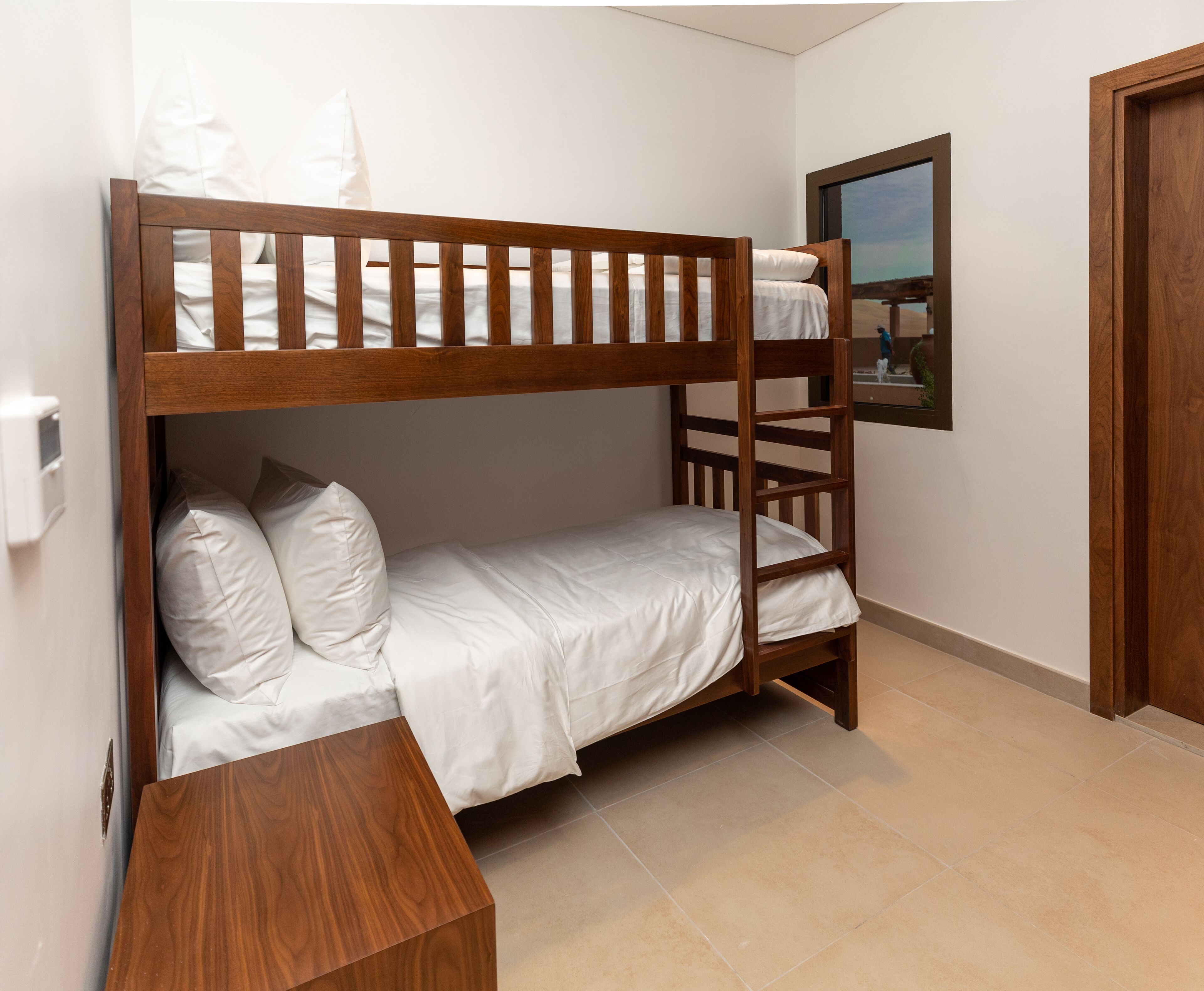A bunk bed with a wooden frame and white bedding in a room with tiled flooring and a door.