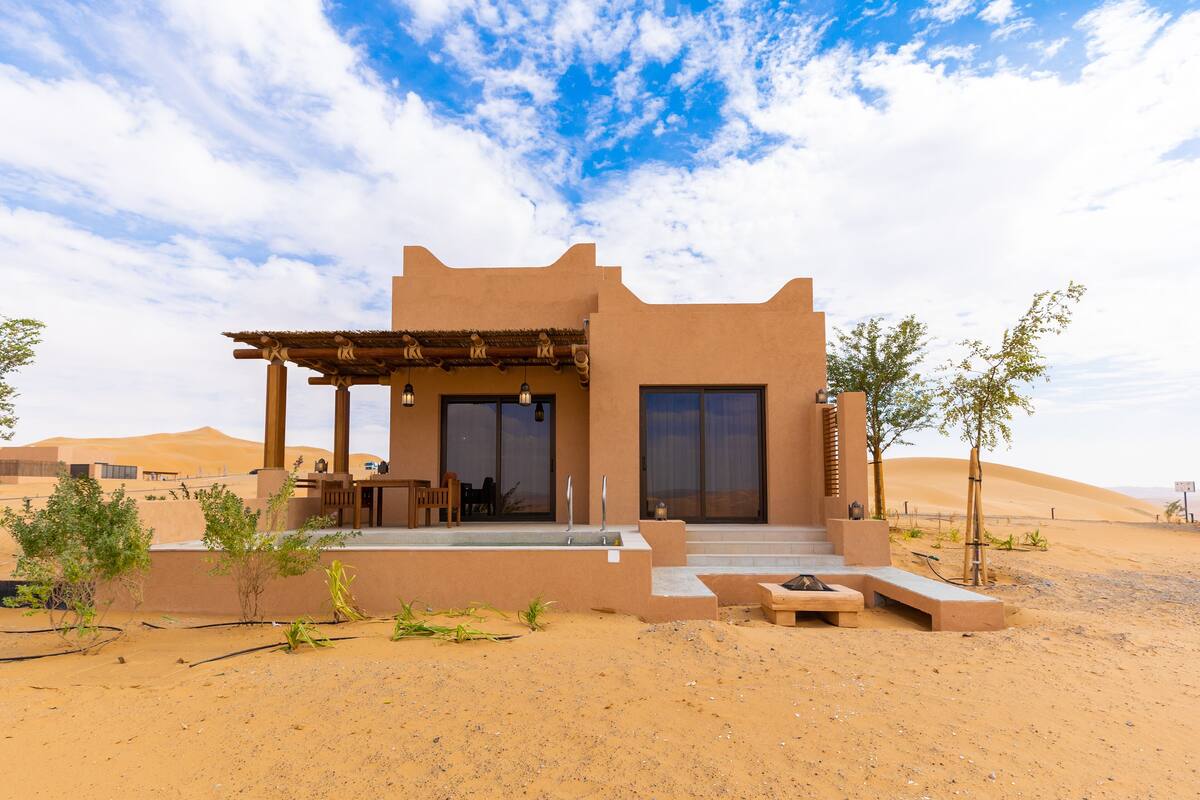 Un bâtiment de style désertique doté d’un patio, de grandes fenêtres et d’une piscine.