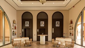 Een receptiegedeelte met een ronde centrale tafel, houten stoelen en drie gewelfde doorgangen met decoratieve patronen.