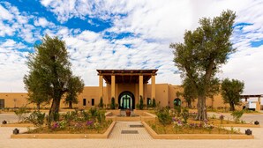 Un bâtiment doté d’une entrée centrale, bordé d’arbres et d’un chemin piétonnier dallé.