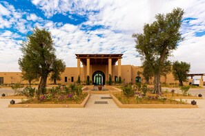 Un bâtiment doté d’une entrée centrale, bordé d’arbres et d’un chemin piétonnier dallé.