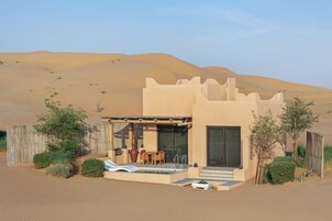 Um resort no deserto com design moderno, apresentando piscina, área de estar externa e vista para dunas de areia.