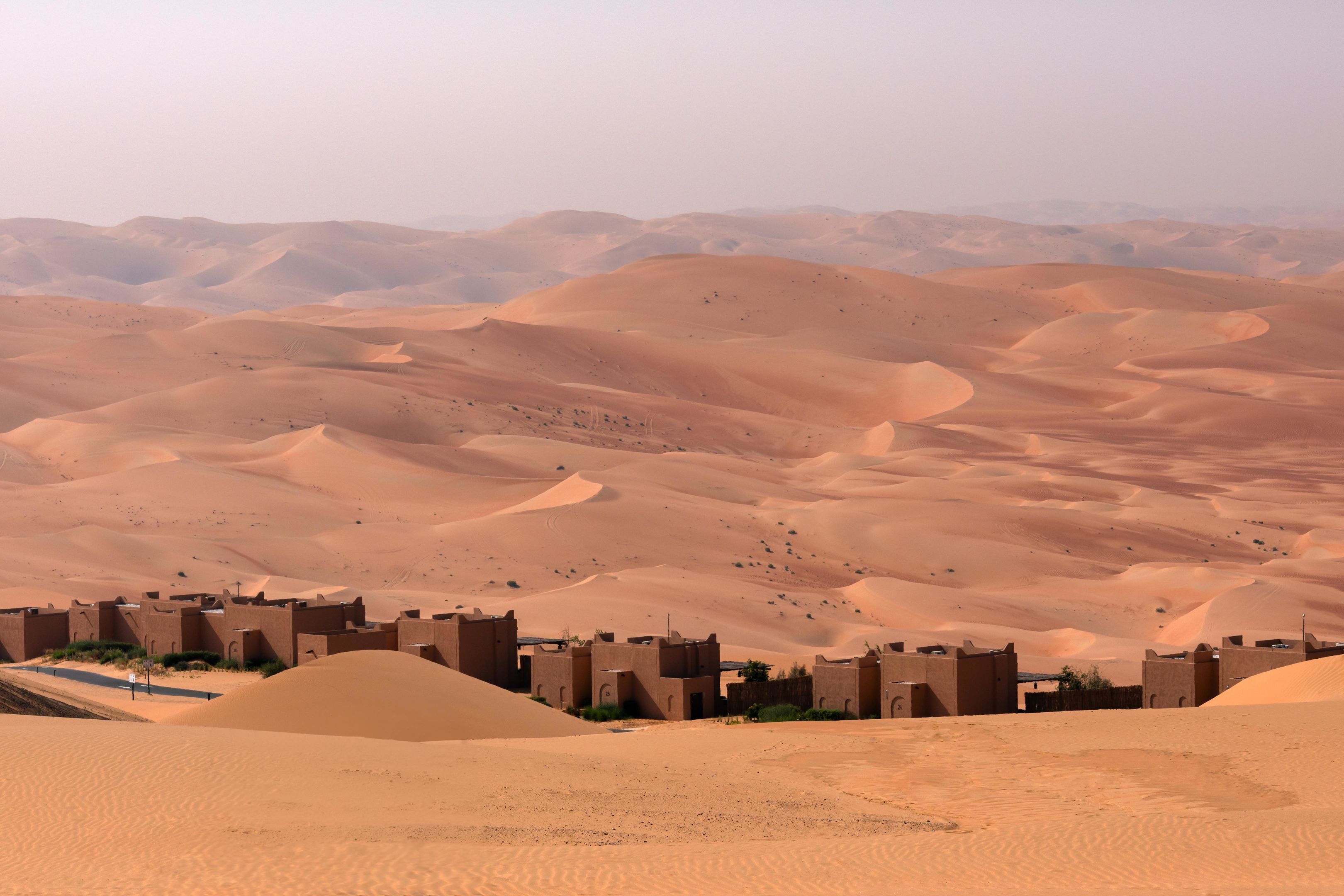 A desert landscape with sand dunes and a small settlement with traditional architecture.