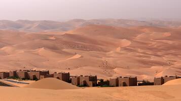 A desert landscape with sand dunes and a small settlement with traditional architecture.