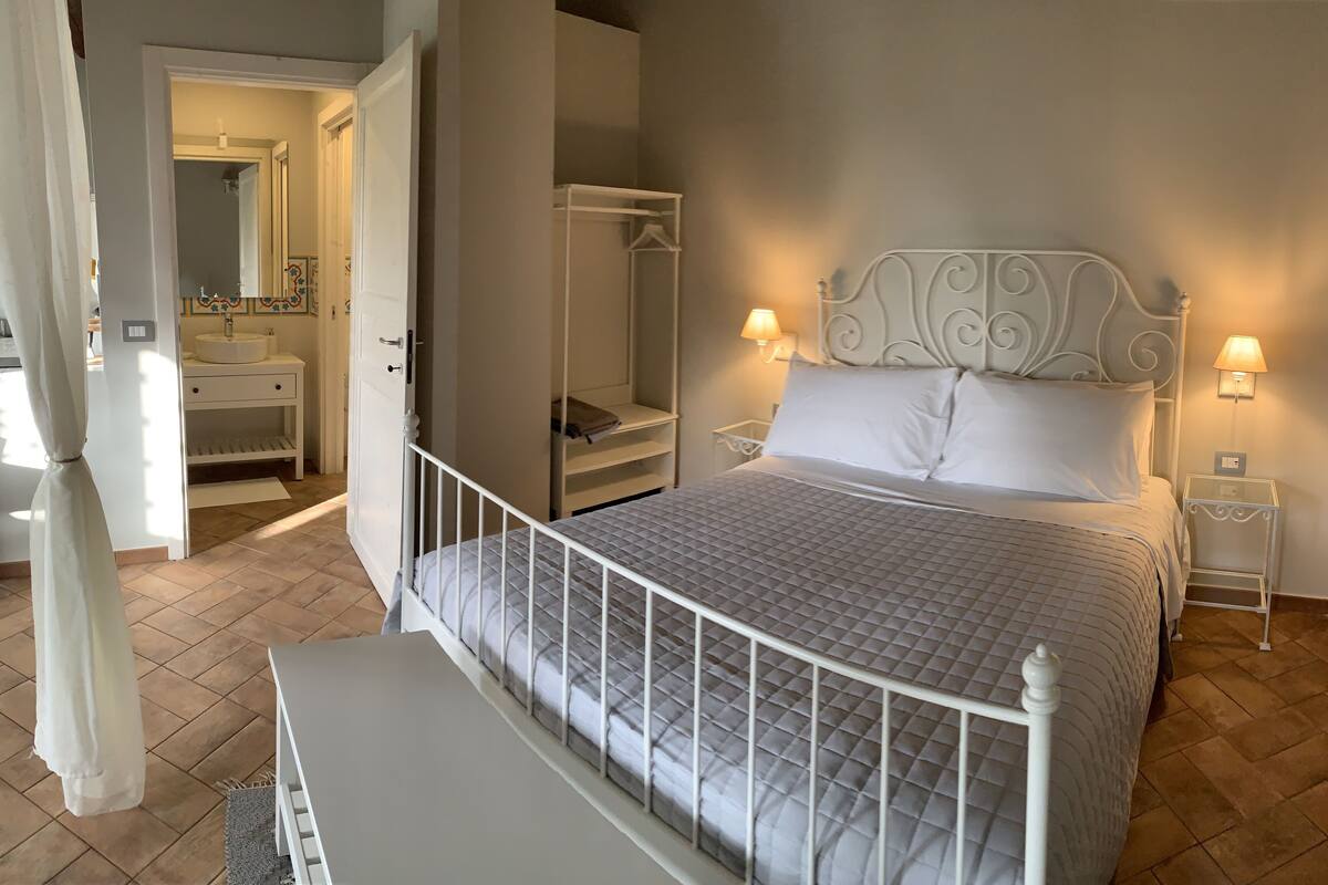 A bedroom with a bed, bedside tables, a wardrobe, and a bathroom visible through an open door.