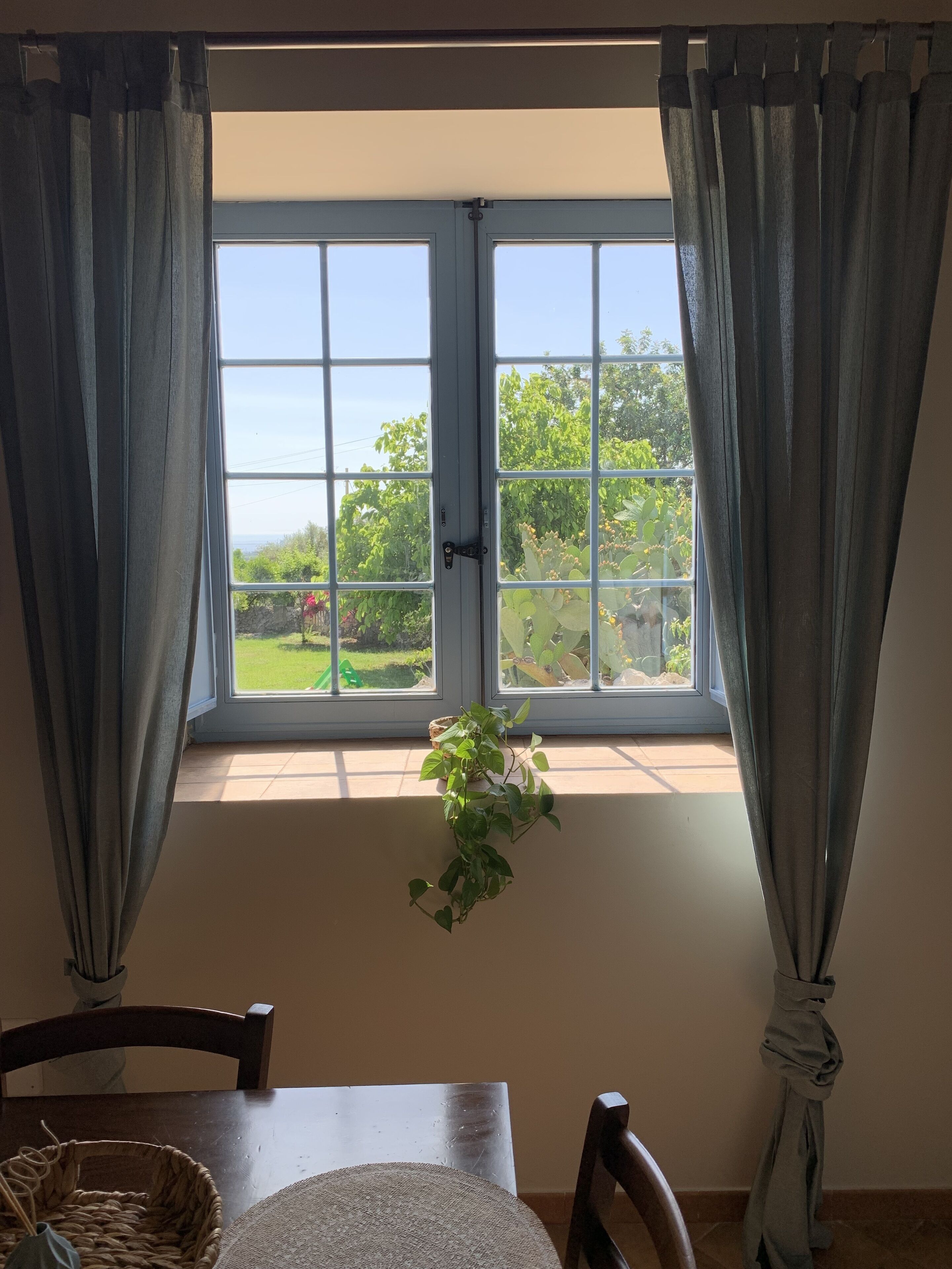 A room with a large window, a hanging plant, and a dining table with chairs.