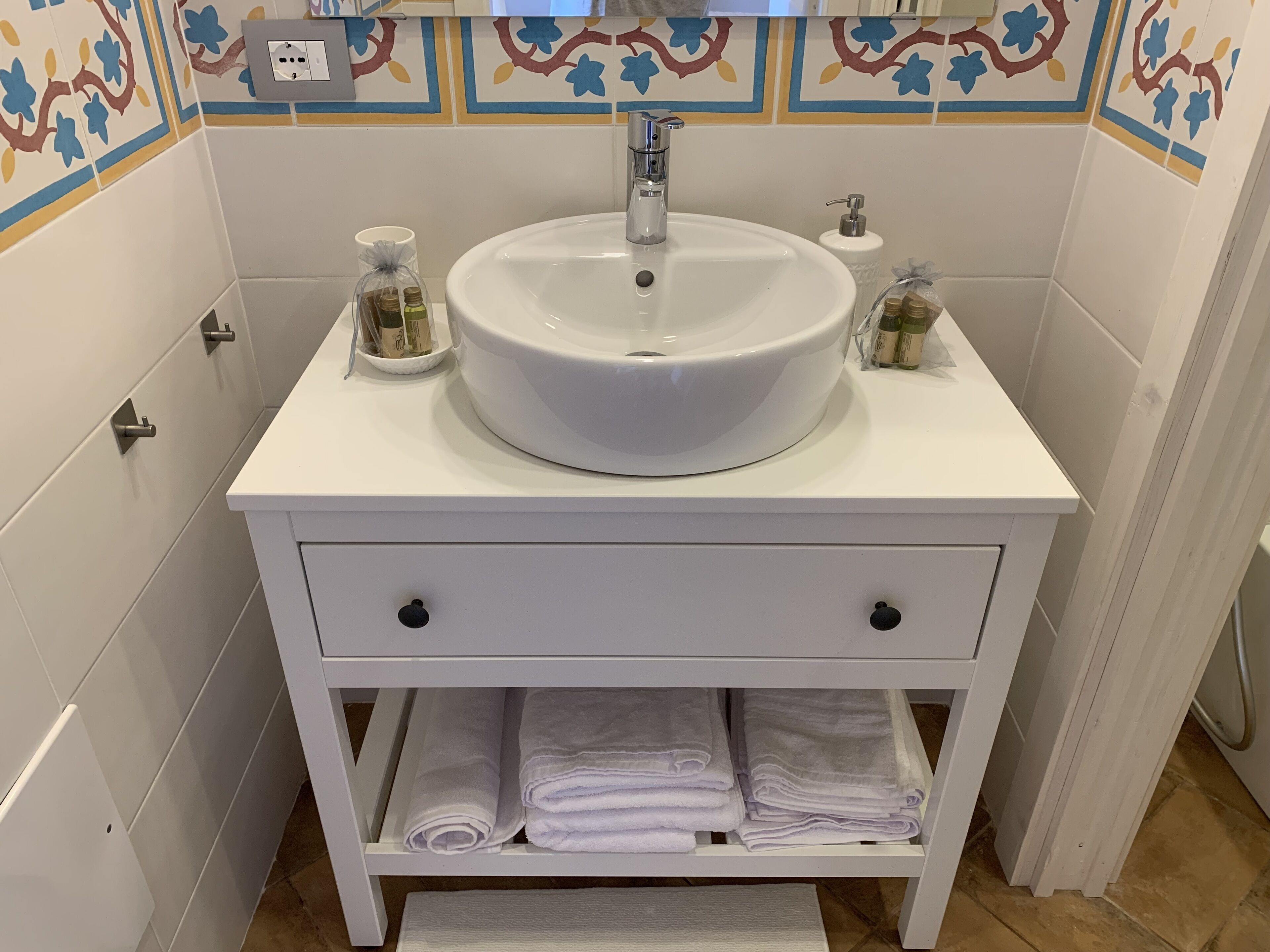 A bathroom with a white sink, two towel racks, and a shelf with folded towels.