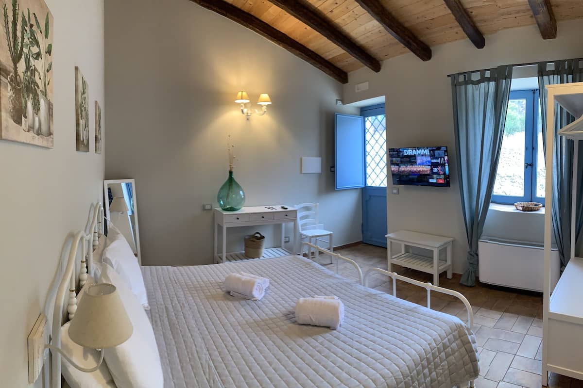 A bedroom with a bed, bedside table, lamp, dresser, mirror, and a television on the wall.