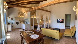 A cozy room with a wooden table, yellow sofa, and a bed with white curtains. - Masseria Santacatrini (Melilli)