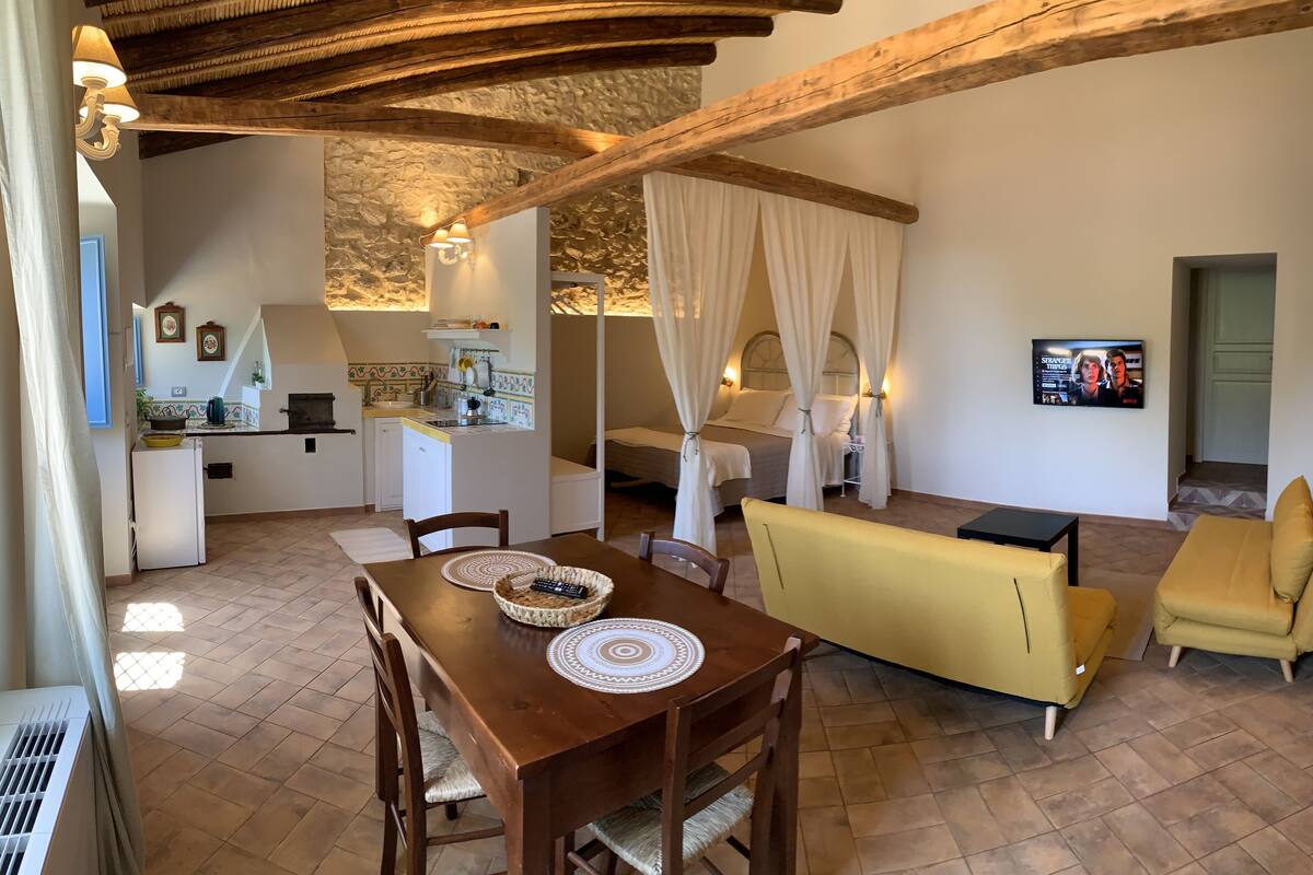 A cozy room with a wooden table, yellow sofa, and a bed with white curtains.