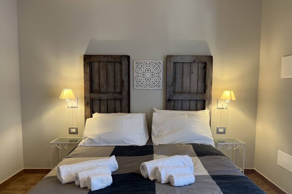 A double bed with a checkered bedspread, two nightstands with lamps, and a decorative wall piece.