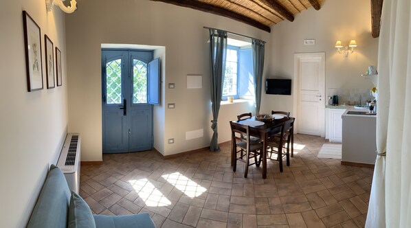 A spacious living area with a dining table, a kitchen with a sink and stove, a large window with curtains, and a door with a lattice design.