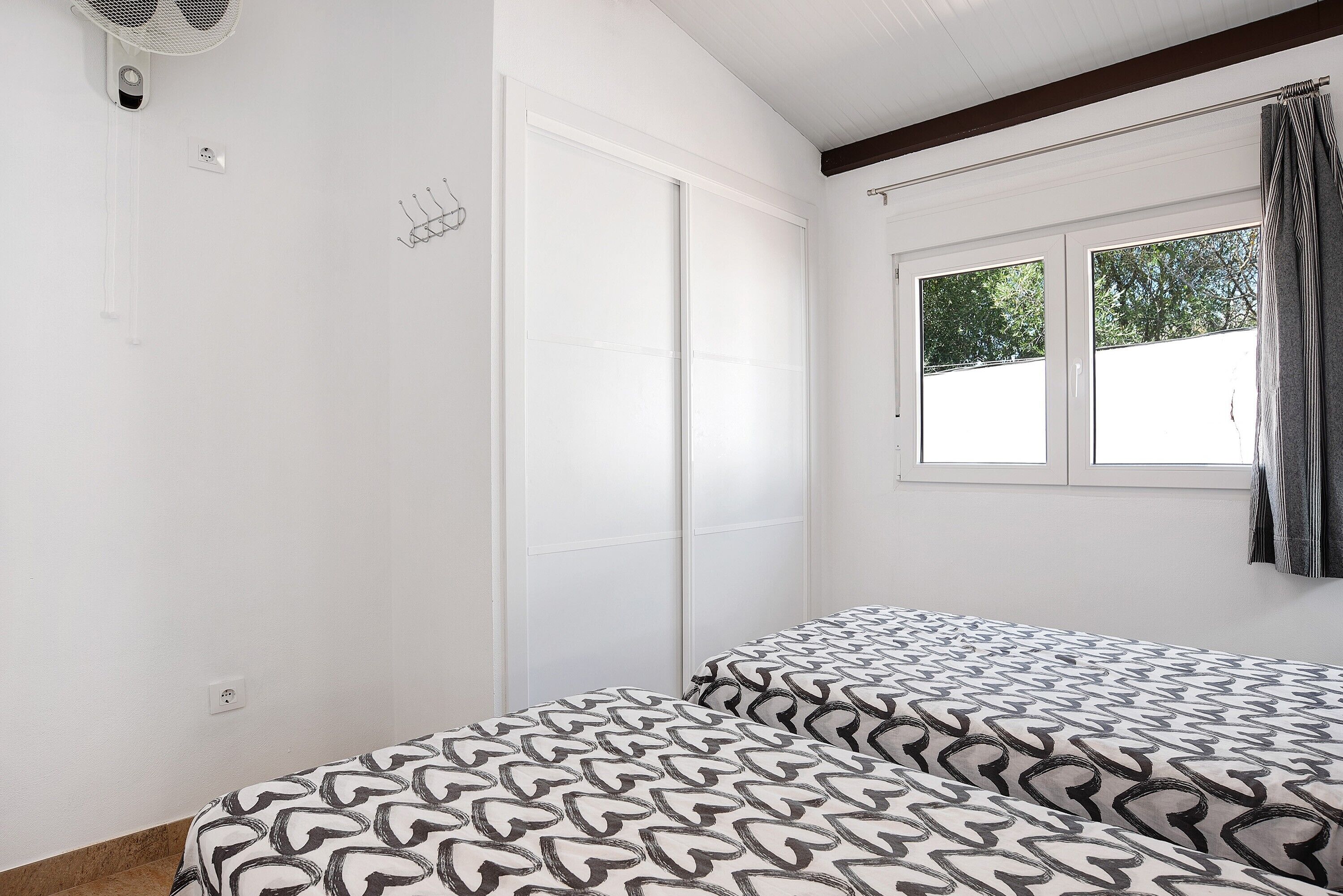 A bedroom with a bed, a window, and a wall-mounted fan.