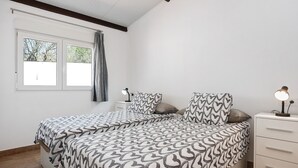 Une chambre avec deux lits, une table de chevet, une lampe et une fenêtre avec un rideau.