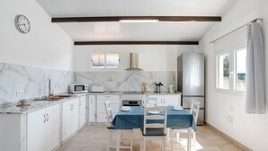 Une cuisine avec des meubles blancs, un four à micro-ondes, une cuisinière et une table à manger pour quatre personnes.