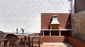 Une terrasse extérieure avec un barbecue en briques, une table dressée pour le repas et des chaises.